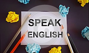 Speak English written on a white paper,Pencils over white paper, crumpled papers page, dark background