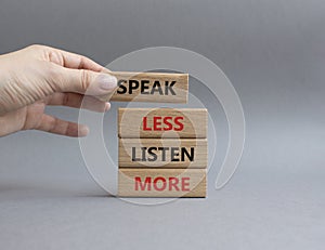 Speak less Listen more symbol. Wooden blocks with words Speak less Listen more. Beautiful grey background. Businessman hand.