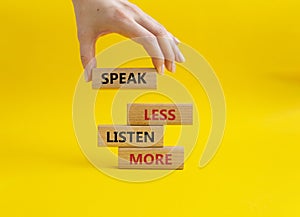 Speak less Listen more symbol. Wooden blocks with words Speak less Listen more. Beautiful yellow background. Businessman hand.