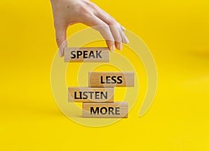 Speak less Listen more symbol. Wooden blocks with words Speak less Listen more. Beautiful yellow background. Businessman hand.