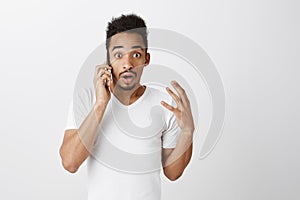 Speak slower, what happened. Indoor shot of nervous shocked attractive guy with afro haircut shaking hand while talking