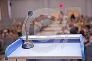 Speaker prepare before speaking to the audience behind the podium focused microphone on the podium and blurred empty seat and some