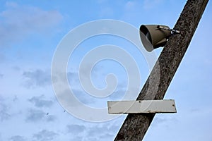 Speaker on a wooden pole with a sign against a blue sky