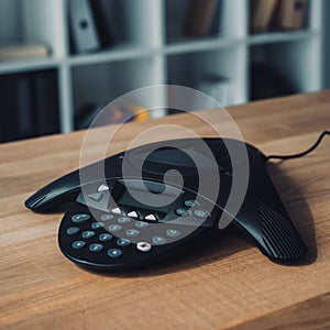 speakerphone on wooden table at office with blurred bookshelves