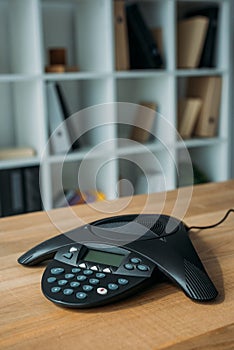 speakerphone on wooden table at office with blurred bookshelves