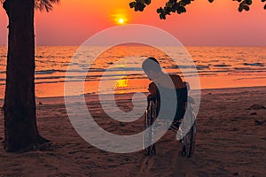 Special child on wheelchair on the sea beach with sunset on travel time