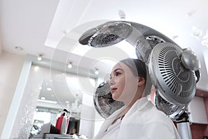 Special equipment for drying hair. A young woman is drying her hair in a beauty salon. The concept of beauty and health.