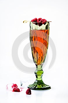 Special green glass with delicious cocktail decorated with raspberries on light background