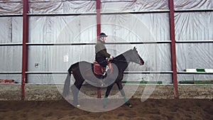 in special hangar, a young disabled man learns to ride a black, thoroughbred horse, hippotherapy. man has an artificial