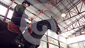 in special hangar, a young disabled man learns to ride a black, thoroughbred horse, hippotherapy. man has an artificial