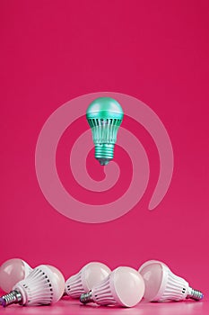 A special Light bulb hovers over simple, standard white light bulbs on a pink background