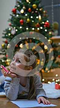 Special orders for Santa. Shot of a beautiful little girl smiling while writing a letter lying near the presents under