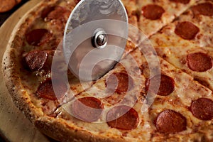 A special pizza knife cuts the pepperoni into pieces. closeup