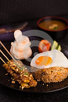 Special rice style of nasi goreng with egg, roasted meat, cracker and vegetables on black platter