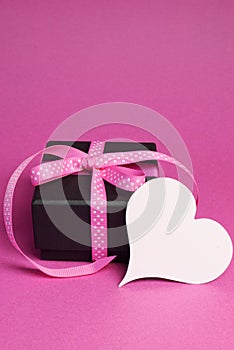 Special small black box present gift with pink polka dot ribbon and white heart shape gift tag - vertical with copy space.