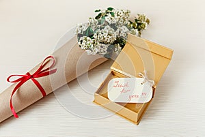 Special Wish Card with Golden Present Box with Bouquet White Small Flowers in Brown Craft Paper.White Wooden Texture Background.