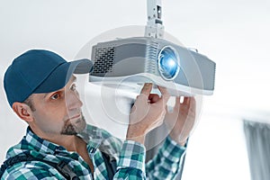 A specialist adjusts the focus of a multimedia video projector for home theater or presentations mounted on a ceiling bracket