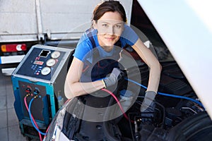 Specialist auto mechanic in overalls refills a car air conditioner