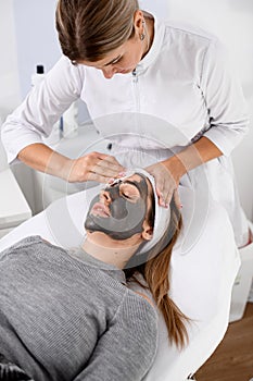 Specialist in the beauty field makes a face mask for a girl with light hair in a beauty salon