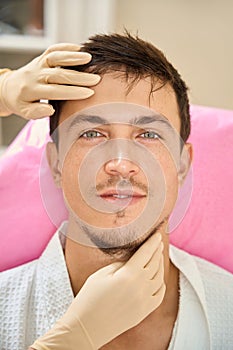 Specialist esthetician examines the face of a brown-haired man