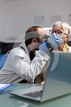 Specialist holding otoscope to do ear examination on senior woman