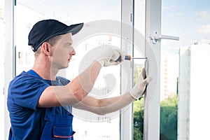 A specialist in installing plastic windows finishes work by screwing additional equipment to the window photo