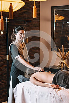 Specialist making hot stone massage to a client. beautiful woman spending time at modern spa cabinet relaxing. Soft