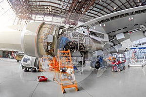 Specialist mechanic repairs the maintenance of a large engine of a passenger aircraft in a hangar. View of engine without bonnet,