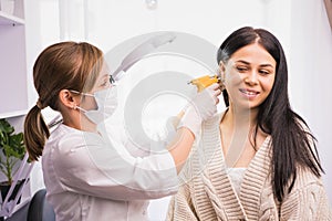 Specialist in medical mask and gloves pierces the client& x27;s ears with a piercing gun in the cosmetologist cabinet.