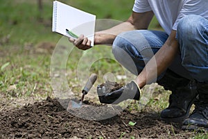 Specialist one hand  checking quality of soil before planting and other hand holding notebook and pen