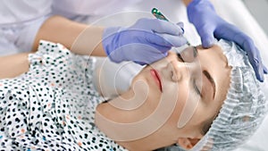 Specialist of permanent make-up create shape of eyebrows using tweezers