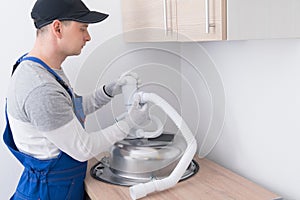 A specialist in protective clothing and gloves, collects and installs a white sewer pipe on a metal sink