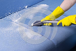 Specialist in protective gloves, cleans the dirty sofa surface with a washing vacuum cleaner and foam, close-up