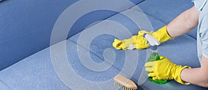 Specialist in protective gloves, cleans the soiled surface of the sofa with foam, a brush and a cloth