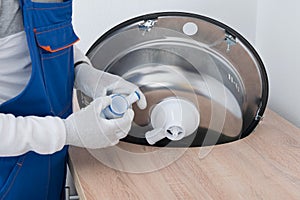 Specialist in protective gloves, installing a sewer pipe on a metal sink, close-up