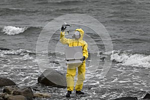 Specialist in protective suit with case and container on rocky shore