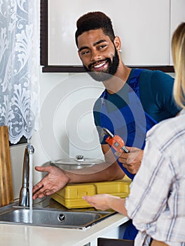 Specialist in uniform fixing leaky faucet, pleased blonde