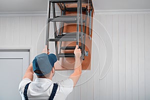 A specialist in uniform folds the attic ladder after installation