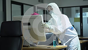 Specialist wearing ppe suit using alcohol sanitizer spray to cleaning computer screen on desk  in office or workplace  against