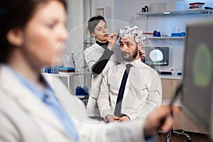 Specialist woman in neuroscience adjusting eeg headset analyzing brain activity of man