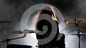 Specially trained girl plays the drums. Black smoke background. Silhouette