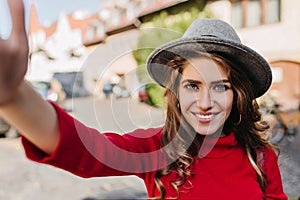 Spectacular blue-eyed white woman in elegant hat making selfie with blissful smile. Refined caucasian female model with