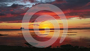 Spectacular drama in the clouds reflected in the sea at sunset, with the silhoutte of a ship in the far distance