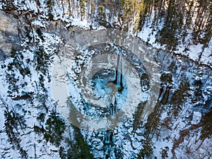 Spectacular drop down view of waterfall falling over rocky forest ledge.