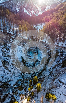 Spectacular drop down view of waterfall falling over rocky forest ledge.