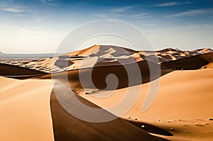 Spectacular large sand dunes of the Erg Chebbi desert in Morocco. Tall sand dunes with wind blowing sand over the top