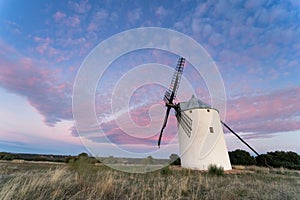 Spectacular lone windmill in the middle of the field at sunset with pink sky.