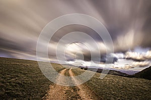 Spectacular long exposure view of clouds above a path on a hill