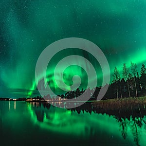 Spectacular night photo strong green lights of dancing Aurora over Northern forest, reflection in lake, small boat, bridge.