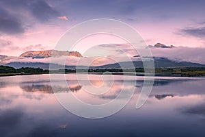 Spectacular reflection of the mountains on a lake with mist under the midnight sun, fairy tale atmosphere in the Vesteralen